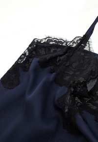 Lingerie en satin bleu foncé avec des délicates bordures en dentelle florale noire et de fines bretelles sur un fond blanc.
