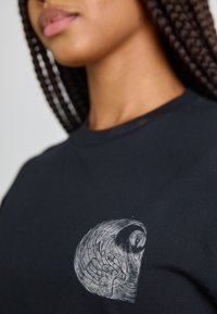 Black cotton t-shirt featuring a gray graphic design of a stylized bird on the left chest area, showcasing intricate detailing and texture.