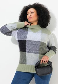 Strick-Pullover mit Rollkragen in grün, schwarz und grau im karierten Muster; gerippter Saum und Bündchen; kombiniert mit einer kleinen schwarzen Handtasche.