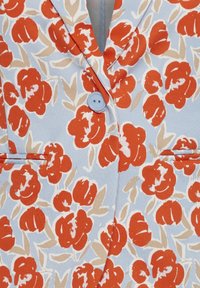 Tissu bleu clair avec un motif floral comprenant de grandes fleurs rouges, des feuilles beiges, et un seul bouton bleu clair au col.