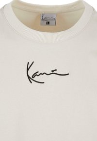 Lys farget hettegenser med ribbet rund hals, med en svart, krumelert brodert logo foran. Mynte, teksturert stoff.