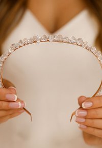 Serre-tête ton or orné de cristaux clairs de forme irrégulière le long du bord supérieur ; finition en métal lisse avec extrémités ouvertes.