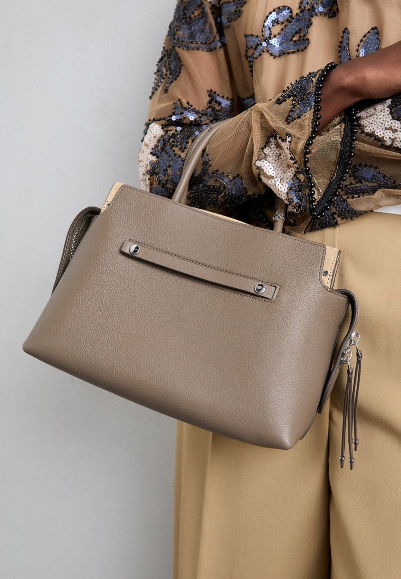 Sac à main en cuir gris avec un design structuré, des poignées supérieures et un compartiment zippé. Présente une sangle frontale minimaliste et des accents en métal.