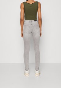 Jeans ajustados grises con una textura desgastada y diseño de cinco bolsillos, combinados con una camiseta sin mangas de canalé en verde oliva. Costuras visibles y detalle en la cinturilla.