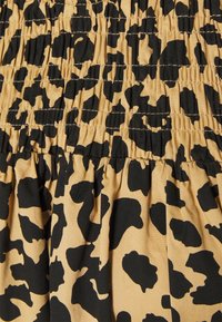 Tkanina s leopardím vzorem, která zobrazuje velké černé skvrny na béžovém pozadí, s nařasenou texturou a sklady.