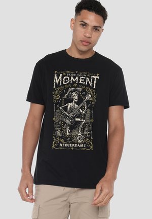 Schwarzes Baumwoll-T-Shirt mit einem grafischen Design eines Skeletts mit einer Gitarre, umgeben von Text und dekorativen Elementen in Gold.