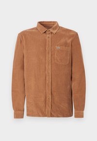 Brown corduroy shirt with a collar, front button placket, and left chest pocket. Features a small green logo on the pocket.