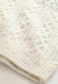 Wool knit hat in cream color with textured, cable-knit pattern and ribbed hem, showcasing soft, fuzzy texture.