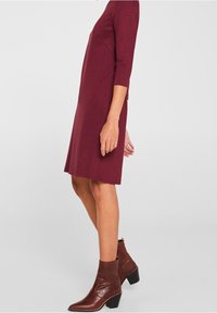 Burgunderfarbenes Kleid mit Dreiviertelärmeln und A-Linien-Schnitt, kombiniert mit braunen Leder-Ankle Boots mit Blockabsatz.