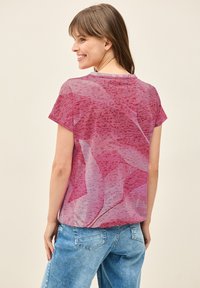 Camiseta de manga corta y cuello redondo en rosa, con un patrón abstracto de hojas texturizado, fabricada con una tela ligera. Corte casual con un ligero brillo.