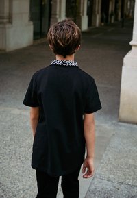 T-shirt nera a maniche corte con colletto nero e bianco a motivo, abbinata a pantaloni neri. Vista da dietro, il tessuto appare liscio.