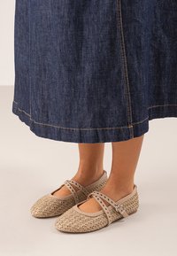 Bailarinas de color beige claro tejidas, con punta redondeada y doble correa ajustable adornada con tachuelas, combinadas con una falda de mezclilla.