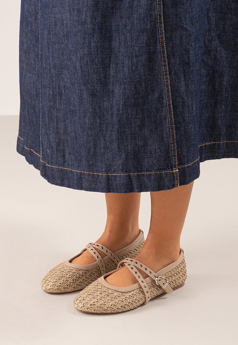 Bailarinas de color beige claro tejidas, con punta redondeada y doble correa ajustable adornada con tachuelas, combinadas con una falda de mezclilla.