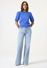 Suéter azul con mangas abullonadas combinado con jeans de corte acampanado de lavado claro. Textura suave con una cintura ajustada; estilo casual y corte holgado.