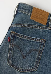 Poche arrière d’un jean Levi’s bleu avec un patch de marque en cuir marron et une étiquette logo en tissu rouge sur le tissu en jean.