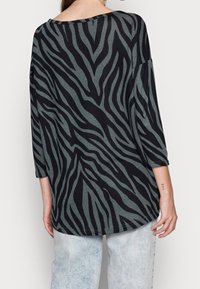 Schwarz- und grau oversized Oberteil mit einem Zebra-Streifenmuster, ausgestattet mit Dreiviertelärmeln und einem weiten Ausschnitt, aus einem weichen Stoff gefertigt.