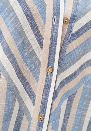 Zbliżenie na pasiasty lniany materiał z beżowymi, niebieskimi i białymi liniami oraz drewnianymi guzikami wzdłuż zapinanej pliski.