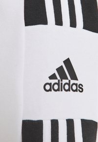 Tela blanca con franjas verticales negras y un logo de Adidas. Textura suave, forma rectangular y diseño de colores contrastantes.