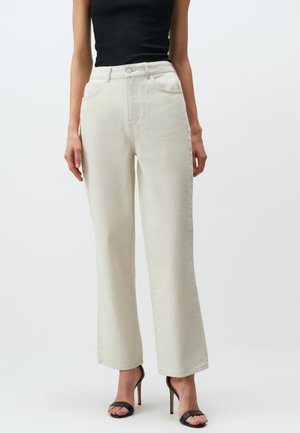 Jean large crème en denim, avec taille haute, poches avant et texture subtile. Accompagné de talons noirs.