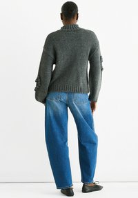 Gray knit sweater with a high collar and puffed sleeves, paired with loose blue jeans. Simple design, textured fabric, and a relaxed fit.