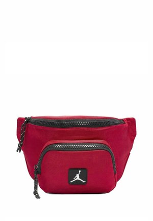 Bolsa de tela roja con dos compartimentos con cremallera, cremalleras negras y un prominente parche del logo de Jordan en negro en la parte frontal. Diseño compacto y funcional.