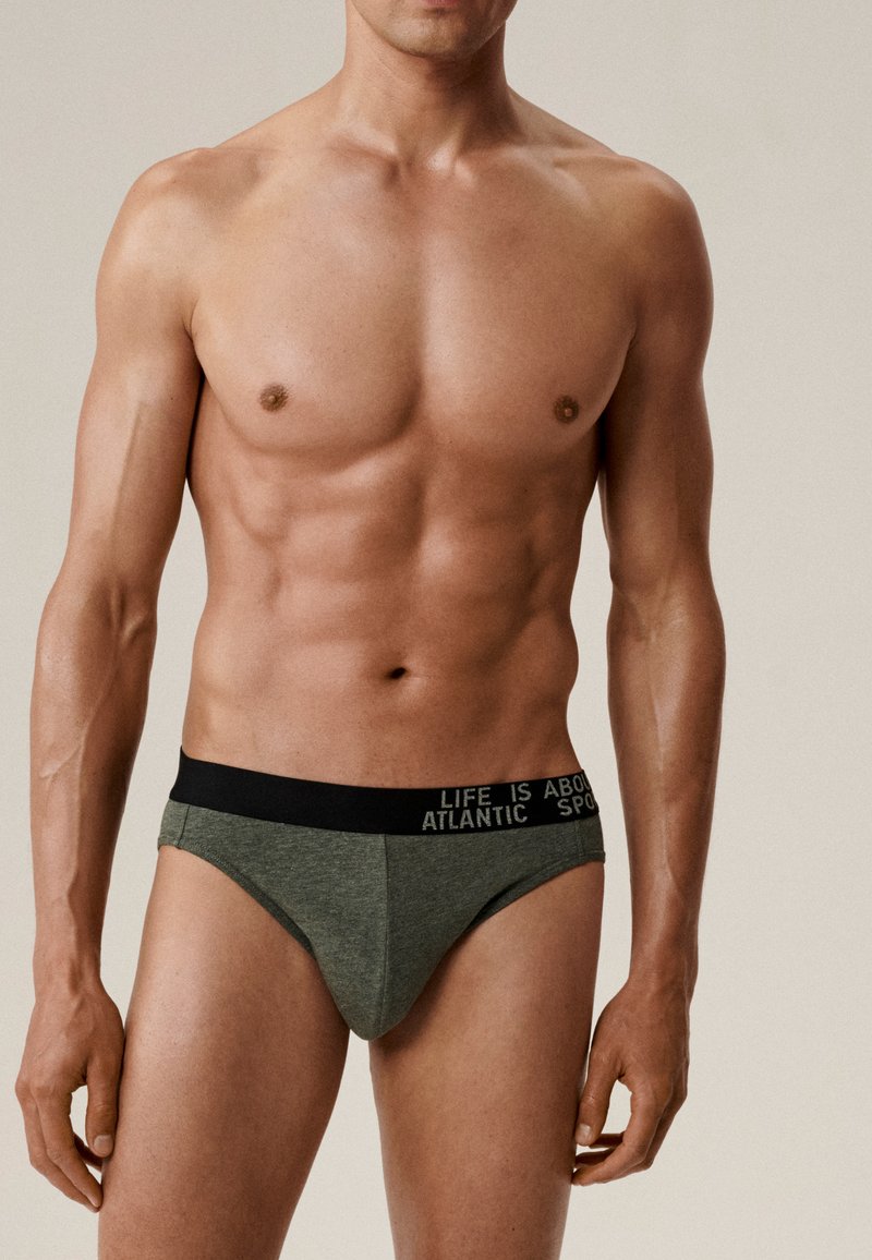 Zielone slipy wykonane z miękkiego materiału z czarnym pasem w talii, na którym znajduje się biały napis. Projekt obejmuje nisko cięty nogawkę i dopasowany krój.