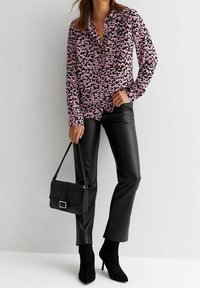 Blus med lång ärm i rosa och svart djurmönster, knäppning fram; matchad med svarta byxor i konstläder och svarta ankelstövlar.