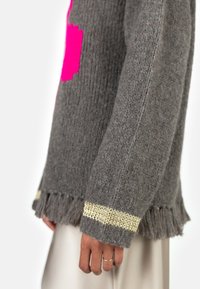Gray knitted sweater with a pink geometric pattern, fringed hem, and a gold-accented cuff. Fabric has a textured look.