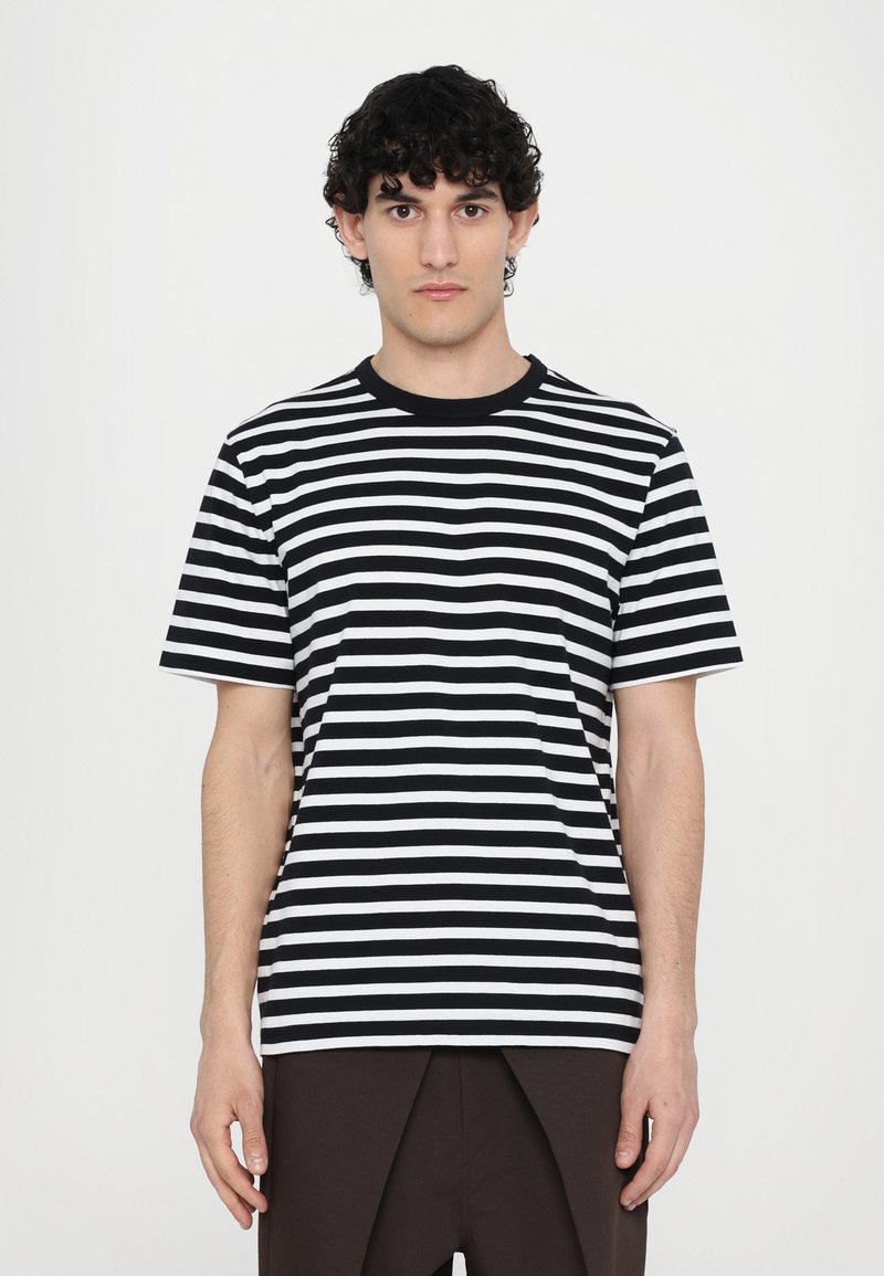 T-Shirt de rayas blancas y negras con mangas cortas y escote redondo, hecha de tela suave, exhibida sobre un fondo neutro.