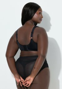 Reggiseno nero con spalline regolabili e chiusura a gancio, abbinato a slip neri trasparenti a vita alta, che mostra una texture liscia.