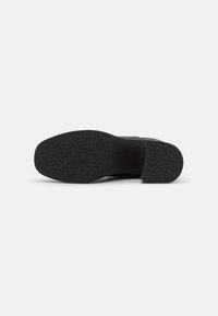 Suela de zapato negra con superficie de goma texturizada, punta redondeada y diseño plano. Sin patrones visibles ni herrajes.