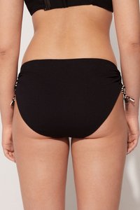 Parte inferior de bikini negra con lados fruncidos y lazos de acento. Tejido texturizado con un acabado suave, que proporciona una apariencia ajustada.