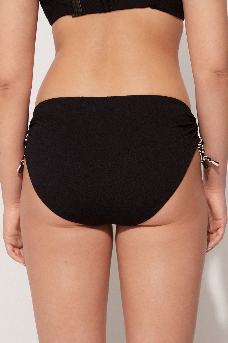 Parte inferior de bikini negra con lados fruncidos y lazos de acento. Tejido texturizado con un acabado suave, que proporciona una apariencia ajustada.