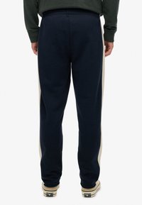 Marineblauwe sweatpants met lichtbeige zijpanelen. Zacht materiaal, elastische tailleband en omgekrulde enkels. Casual pasvorm voor comfort en bewegingsvrijheid.