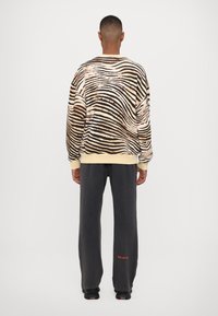 Överdimensionerad sweatshirts med beige och svarta vågiga ränder; ribbat nacke och ärmslut. I kombination med mörkgrå träningsbyxor med röd text.