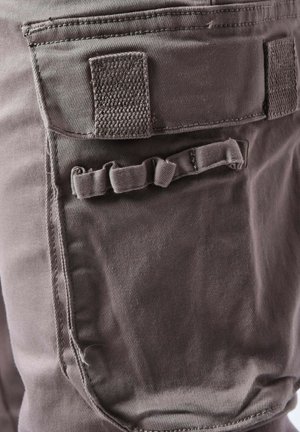 Tejido de color gris oscuro con una textura suave, que presenta un bolsillo trasero rectangular y un pequeño detalle en forma de lazo para sujeción.