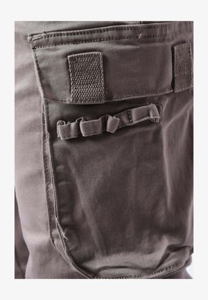 Tejido de color gris oscuro con una textura suave, que presenta un bolsillo trasero rectangular y un pequeño detalle en forma de lazo para sujeción.