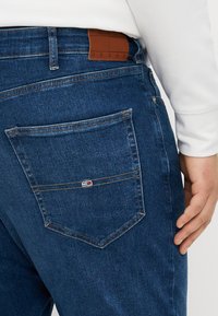 I jeans in denim blu scuro presentano una tasca posteriore con un piccolo logo del marchio, un'etichetta in pelle marrone sulla vita e cuciture ben rifinite.