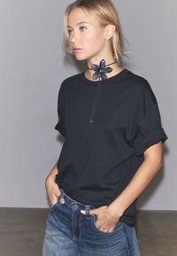 Svart kortärmad sweatshirt kombinerad med blå jeans i denim. Ett dekorativt svart blommönstrat chokerhalsband pryder halsringningen.