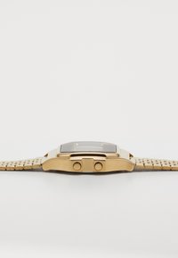 Goldfarbene Uhr mit rechteckigem Gehäuse, dunklem Zifferblatt und einem strukturierten Metall-Mesh-Armband. Enthält zwei Druckknopfkrone an der Seite.