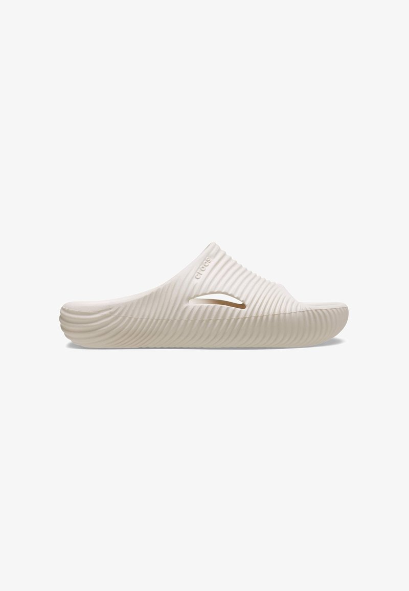 Helle beigefarbene Slip-On-Sandale mit gerillter Oberfläche, abgerundeter Spitze und seitlichen Belüftungslöchern; aus flexiblem Material gefertigt.