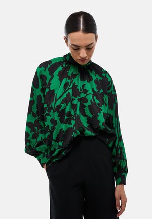 Blouse à motif floral vert et noir avec un col haut, des manches longues et une coupe ample, associée à un pantalon noir. Texture lisse.