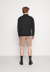 Sudadera negra con un cuello alto, pantalones cortos beige, calcetines oscuros y zapatos negros. Tejido suave con un diseño ajustado, visto desde la espalda.