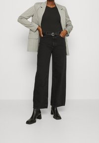 Svarta vida jeans med en strukturerad yta, i kombination med en grå kavaj med fickor och svarta klackade ankelstövlar. Enkel svart t-shirt med v-ringning.