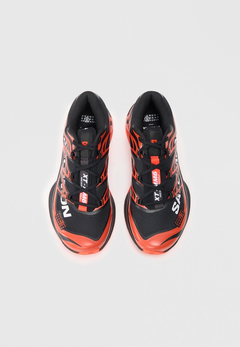 Sorte og orange sportssko med mesh-overdel, tekstureret design, snørebånd og dynamiske brandingdetaljer på siderne og på tungen.