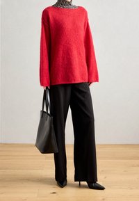 Persona che indossa un maglione rosso morbido sopra un dolcevita a righe bianche e nere, pantaloni larghi neri, tacchi a punta neri, mentre tiene una borsa a tracolla nera.