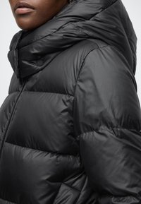 Czarna kurtka puchowa z wysokim kołnierzem, zapinana na zamek błyskawiczny, z pikowanym wzorem. Wykonana z gładkiego, błyszczącego materiału o matowym wykończeniu.