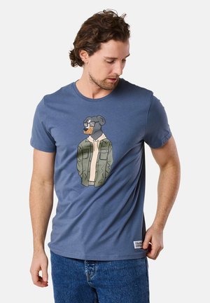 T-shirt di cotone blu con grafica di un cane con occhiali da sole e giacca verde. Collo rotondo e vestibilità rilassata con maniche corte.