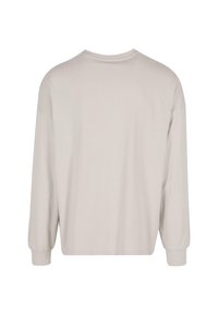 Camisa de manga larga color beige claro con cuello redondo, hombros caídos y puños elásticos. Textura suave y corte relajado.
