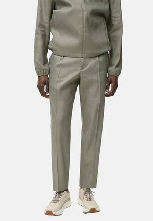 Giacca di felpa verde oliva con polsini elasticizzati abbinata a pantaloni a sigaretta coordinati. Accentuata con sneakers beige con suole testurizzate.
